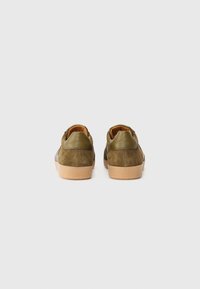 Baskets en suede vert avec semelles en caoutchouc beige ; dotées d'un accent en cuir lisse au niveau du talon, conçues avec un profil bas et une forme arrondie.