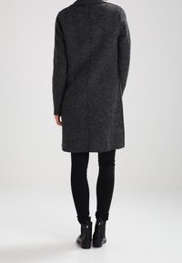 Cappotto grigio in lana con taglio dritto, maniche lunghe e colletto a giacca, abbinato a leggings neri e stivaletti alla caviglia.