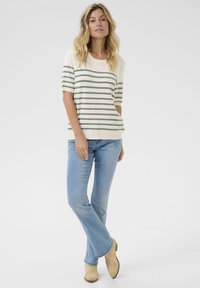 Gestreepte top met korte mouwen in crème en gedempt groen, gecombineerd met lichtblauwe jeans en beige enkellaarsjes, met een ontspannen pasvorm.