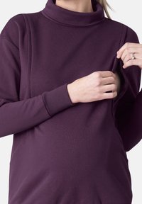 Fialová mikina s vysokým límcem a bočním zipem; vyrobena z měkké látky. Má uvolněný střih, ideální pro pohodlí a snadné nošení.