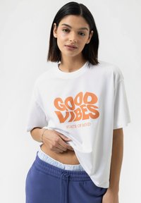 Witte katoenen T-shirt met een oversized pasvorm, voorzien van een gedurfde oranje graphic met de tekst "GOOD VIBES STATE OF MIND" op de voorkant.