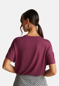 Bordové tričko s krátkým rukávem, uvolněný střih, kulatý výstřih a hladká textura, kombinované s vzorovanou sukní s modrými, černými a bílými akcenty.