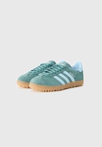 Baskets de sport en daim vert avec des accents bleu clair, trois bandes blanches et une semelle en caoutchouc beige. Présentent une pointe arrondie et un design à lacets.