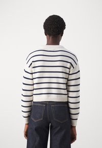 Pull en maille crème avec des rayures bleu marine, doté d'un col rond et d'un ourlet côtelé. Le mannequin porte un jean bleu foncé.