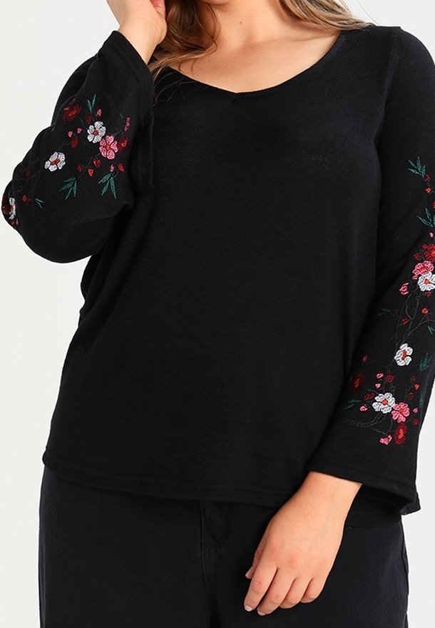 Haut noir à manches longues avec broderie florale rouge et blanche sur les manches. Col en V, coupe décontractée et texture douce.