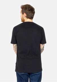 Schwarzes Baumwoll-T-Shirt mit Rundhalsausschnitt, kurzen Ärmeln und geradem Schnitt. Hat einen schlichten Rücken und wird mit blauen Jeans kombiniert.