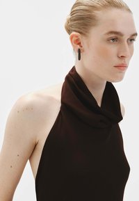 Top halter de cuello de cowl marrón con una textura suave. Pendientes geométricos negros, de diseño minimalista. Enfoque en los detalles del escote y los hombros.
