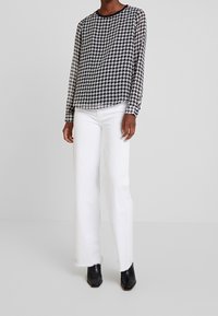Maglia a maniche lunghe bianca e nera a motif houndstooth abbinata a jeans bianchi a gamba larga. Completata con stivaletti neri e scollatura rotonda.