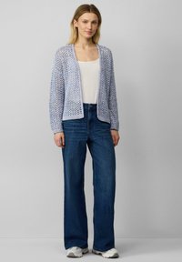Hellblauer gestrickter Cardigan mit offenem Frontbereich, strukturiertem Muster und langen Ärmeln, kombiniert mit weißem Oberteil und dunkelblauen, weit geschnittenen Jeans.