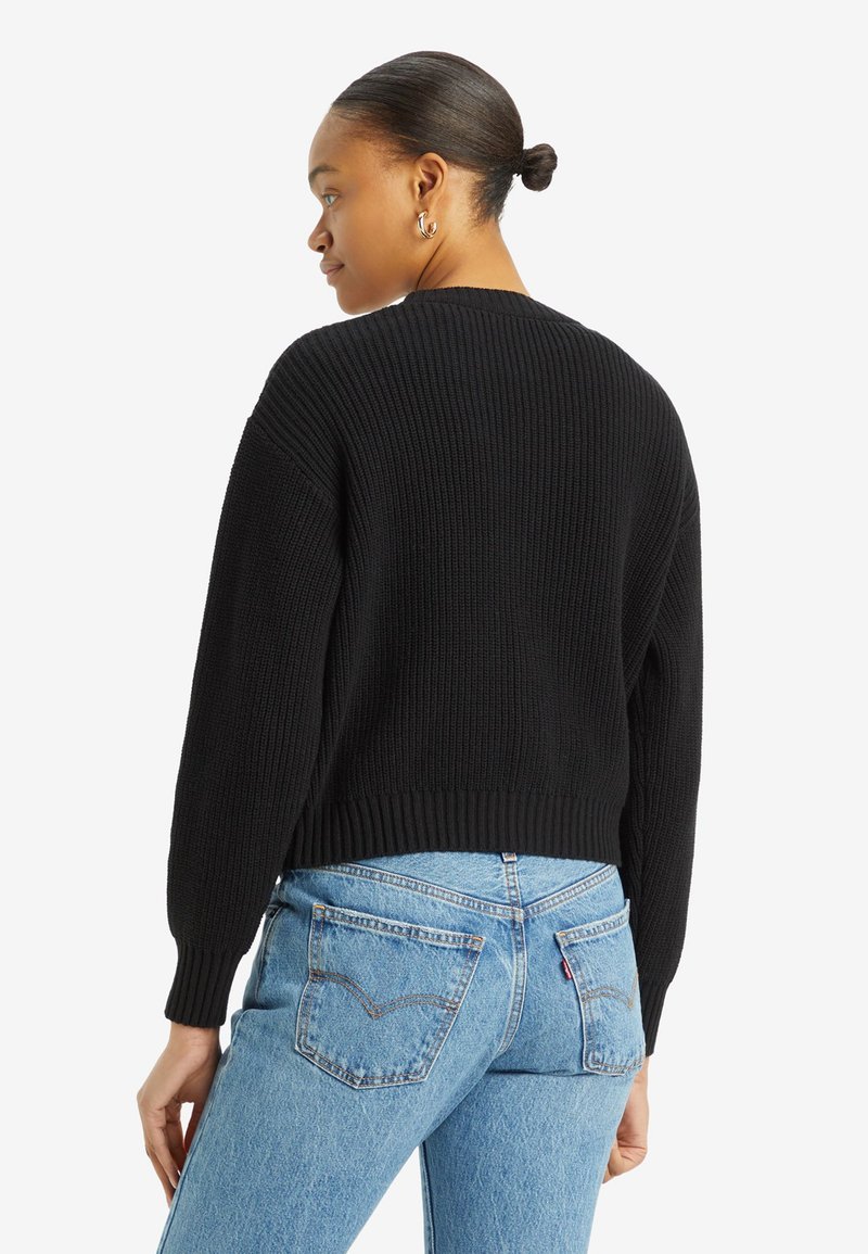 Pull en tricot noir à côtes avec un design court et des manches longues, associé à un jean taille haute bleu clair avec des poches arrière.