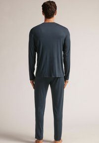 Donkergrijze pyjama-top met lange mouwen en bijpassende broek in een zachte, gladde stof, met een relaxed fit en zonder zichtbare patronen of accenten.