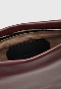 Viininpunaisen nahkalaukun sisäpuoli, jossa on sileä pinta, esittäen vetoketjua, jossa on kultaiset metalliosat ja vaalea vuori. Musta etiketti näkyvissä sisällä.