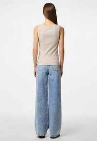Luźne, jasnoniebieskie dżinsy o szerokich nogawkach, w połączeniu z dopasowanym beżowym topem bez rękawów o prążkowanej fakturze i okrągłym dekolcie.