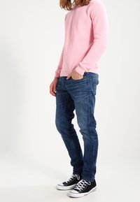 Ljusrosa texturerad långärmad skjorta, blå slim-fit jeans och svarta canvas sneakers med vita sulor. Avslappnad outfit utan synliga logotyper.