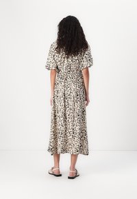 Leopardmønstret kjole med korte puffærmer, elastisk talje, flydende midi-længde, beige og brune farver, parret med flade sandaler.