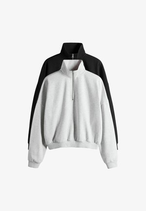 Dvi pusiau užtraukiamos sportinės palaidinės sustumtų viena ant kitos, viena šviesiai pilka priekyje, o kita juoda gale, abi su aukštais apykakliais ir ribotais rankogaliais bei apačiomis.