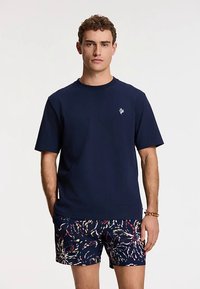 Tmavomodré bavlnené tričko s krátkymi rukávmi a okrúhlym výstrihom, doplnené vzorovanými plavkovými šortkami s viacfarebným abstraktným vzorom.