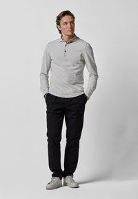 Graues Langarm-Polohemd mit drei Knöpfen, kombiniert mit dunklen Hosen und weißen Sneakers. Minimalistisches Design und glatte Textur.