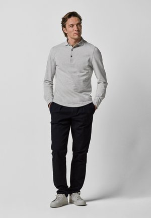 Grå långärmad polo skjorta med tre knappar, i kombination med mörka byxor och vita sneakers. Minimalistisk design och slät textur.