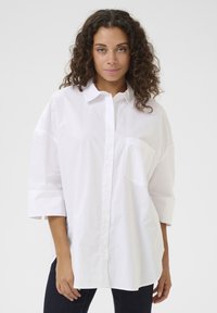 Camicia bianca in cotone con taschino sul lato sinistro del petto, vestibilità oversize e maniche a tre quarti.