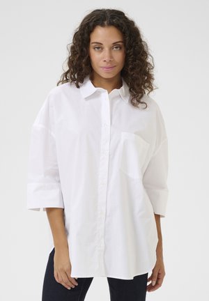 Camicia bianca in cotone con taschino sul lato sinistro del petto, vestibilità oversize e maniche a tre quarti.