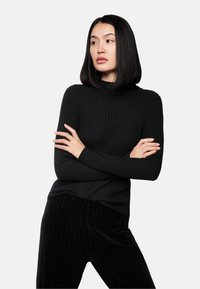 Schwarzer gerippter Rollkragenpullover mit langen Ärmeln, kombiniert mit schwarzen, gestreiften Samthosen. Glatte Textur und figurbetonte Silhouette.