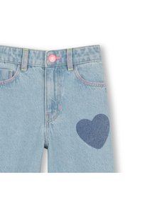 Ανοιχτό μπλε τζιν παντελόνι με σκούρο μπλε μπαλώμα σε σχήμα καρδιάς στο αριστερό πόδι, με ροζ ραφές και ροζ κουμπί στη μέση.