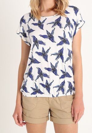 Witte T-shirt met blauw bloemenpatroon, korte omgeslagen mouwen, relaxte pasvorm, gecombineerd met beige shorts. Katoenen materiaal, gladde textuur.