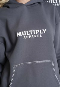 Szara bluza z kapturem z przednią kieszenią, z białym napisem "MULTIPLY APPAREL". Kieszeń ma kontrastowe białe akcenty w szwach.