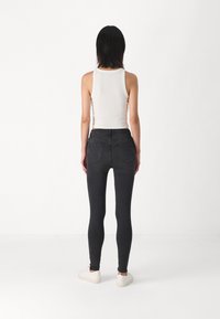 Crne skinny traperice s visokim strukom, stražnjim džepovima i glatkom teksturom; kombinirane s pripijenim bijelim majicom na tajice i bijelim tenisicama.