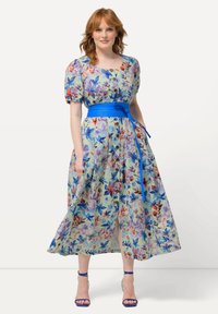 Květinové maxi šaty z světle modré tkaniny s živými multicolor květinami, krátkými puff rukávy a širokým modrým páskem podtrhujícím pas.