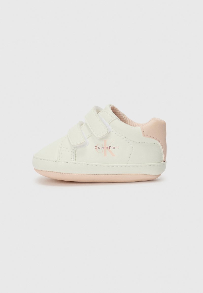 Baskets en faux cuir blanches avec deux bandes auto-agrippantes, accent de talon rose doux, et un logo rose et blanc sur le côté. Design à bout rond.
