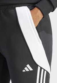Pantalons de sport noirs avec panneaux latéraux blancs. Dotés d'une taille élastique, d'une poche et d'un logo Adidas blanc. Tissu texturé, design sportif.