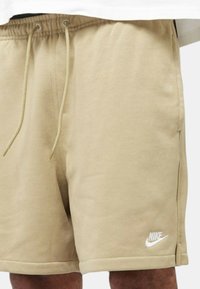 Pantaloni sportivi beige realizzati in morbido misto cotone. Presentano una cintura elastica con cordino e il logo bianco Nike sul lato sinistro in basso.