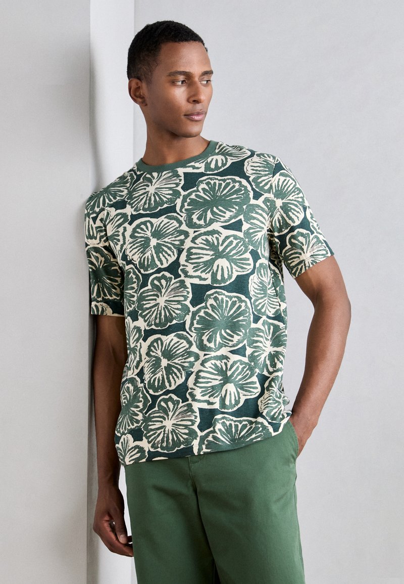 Green short-sleeve t-shirt featuring a floral pattern with white outlines, made from textured fabric, paired with green pants.