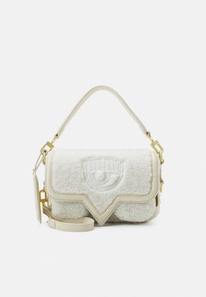 Small cream-colored handbag with textured fabric, flap closure featuring an embossed eye design, and gold hardware accents.
