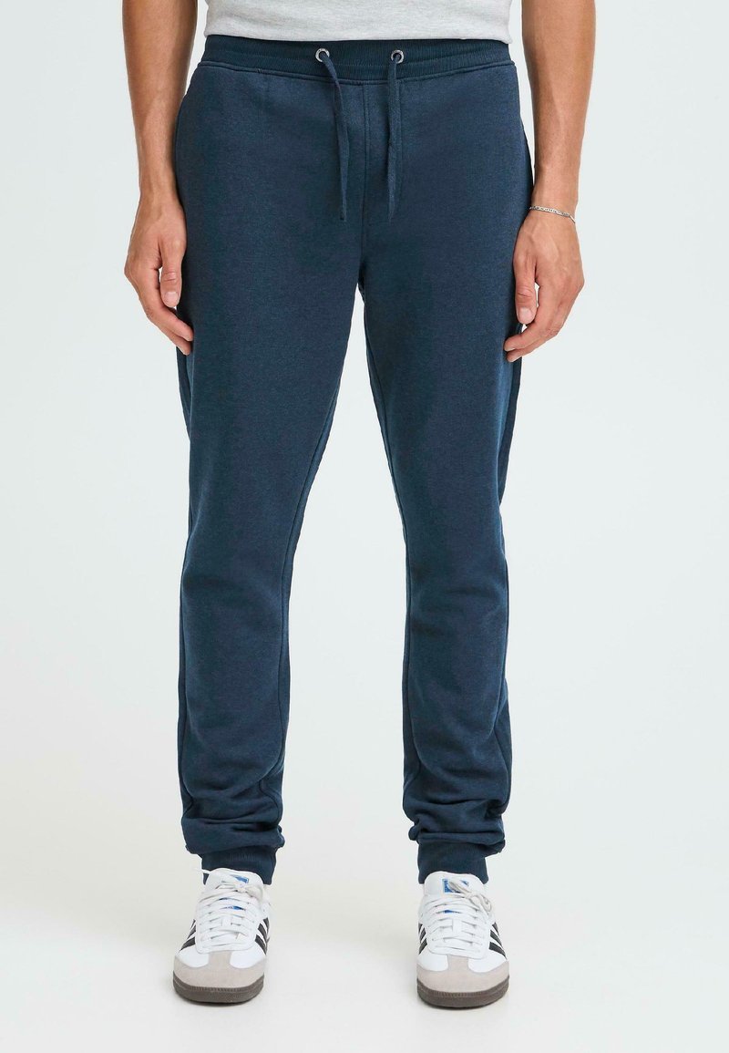 Marineblauwe joggingsbroek van zacht materiaal, voorzien van een elastische tailleband met trekkoord, geborduurde enkels en zijzakken.