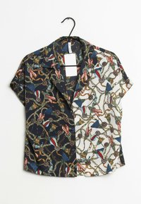 Blusa a maniche corte con un design a spacco: un lato presenta un motivo floreale scuro, l'altro un motivo a catena chiara, entrambi con colori vivaci.