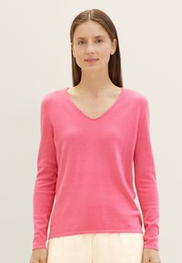 Pull rose à col en V avec manches longues, fabriqué dans un matériau doux, présentant une coupe ajustée et une texture lisse.