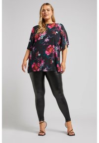 Top con stampa floreale nera con maniche corte e trasparenti, abbinato a leggings neri lucidi e sandali neri con cinturini.