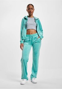 Turkusowy komplet dresowy z weluru, składający się z bluzy z zamkiem błyskawicznym, mającej dwie przednie kieszenie oraz zwężanych spodni z elastycznym pasem i bocznymi kieszeniami.
