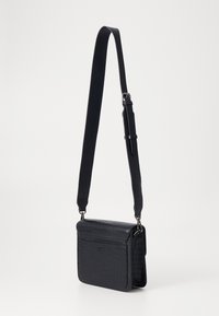 Svart läder crossbody-väska med ett texturerat krokodilmönster, justerbar rem och framflap med logodetalj. Rektangulär form.