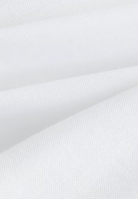 Tissu blanc texturé en plis, présentant un motif délicat et subtil ainsi qu'une surface lisse, exhibant des reflets de lumière et de la profondeur.