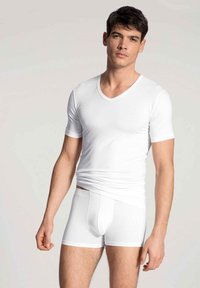 Weißes Baumwoll-V-Ausschnitt-T-Shirt mit kurzen Ärmeln, kombiniert mit weißen Boxershorts. Glatte Textur und taillierter Schnitt, der einen schlichten Stil präsentiert.
