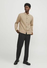 Bežinė mygtukinė marškiniai su tekstūruota raštu, derinami su tamsiomis kelnėmis ir juodais batais. Yra klasikinis apykaklė ir tiesios kirpimo dizainas.