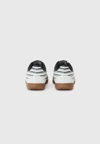 Zapatillas deportivas blancas con detalles en negro y textura a rayas, con una suela de goma marrón y tacón redondeado.