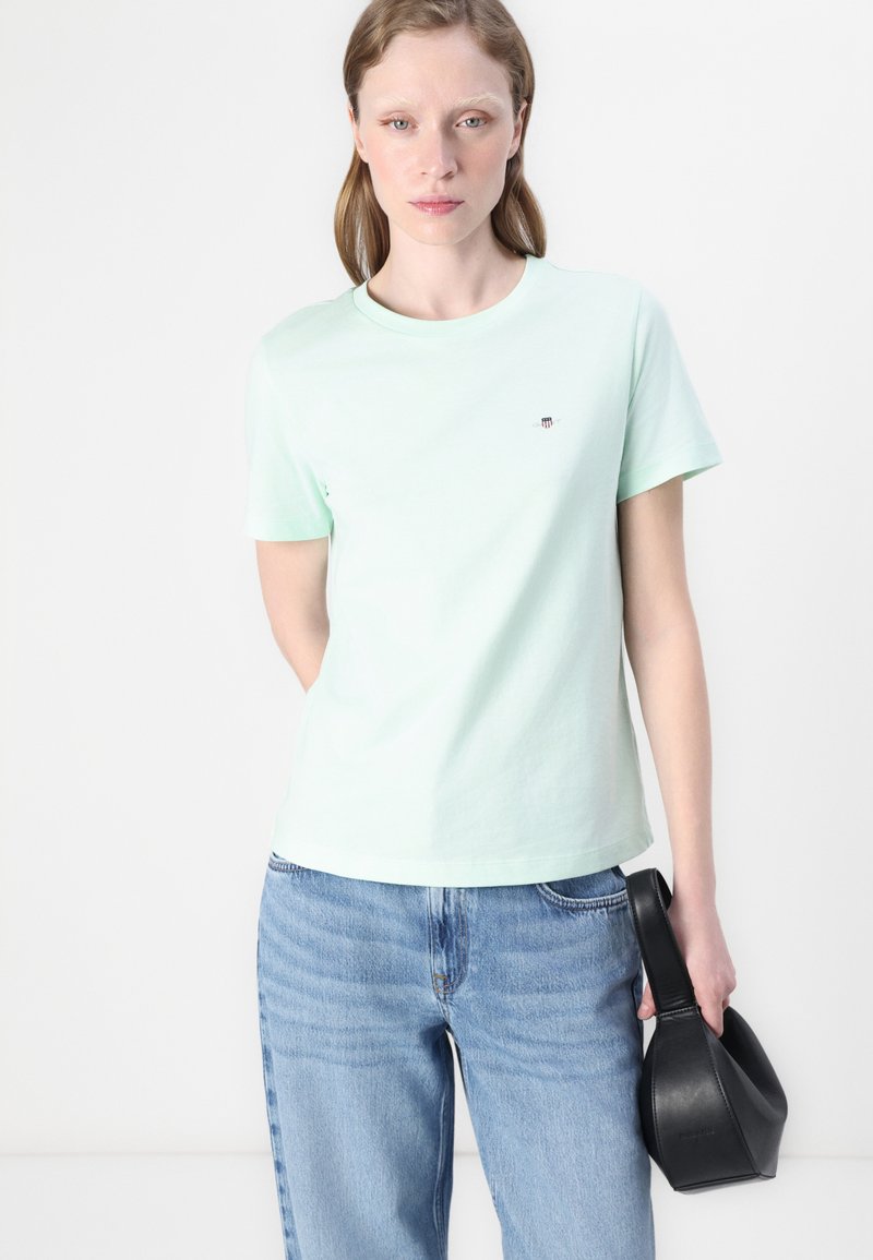 Mintgroene katoenen t-shirt met een ronde halslijn, korte mouwen en een klein logo op de borst. Gecombineerd met blauwe denim jeans en een zwarte handtas.