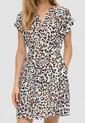 Frau trägt ein kurzärmeliges, tailliertes Kleid mit mehrfarbigem Leopardenmuster in Schwarz, Orange und Hellblau auf weißem Hintergrund.