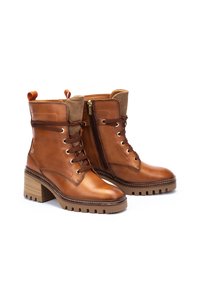 Botas de tobillo de cuero marrón con un acabado texturizado, diseño de cordones, herrajes dorados, cremallera lateral y tacón bloque para mayor estabilidad.