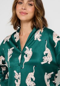 Camicia in satin verde con un motivo giocoso di tigri rosa e crema. Il tessuto ha una texture liscia e un design di colletto classico.